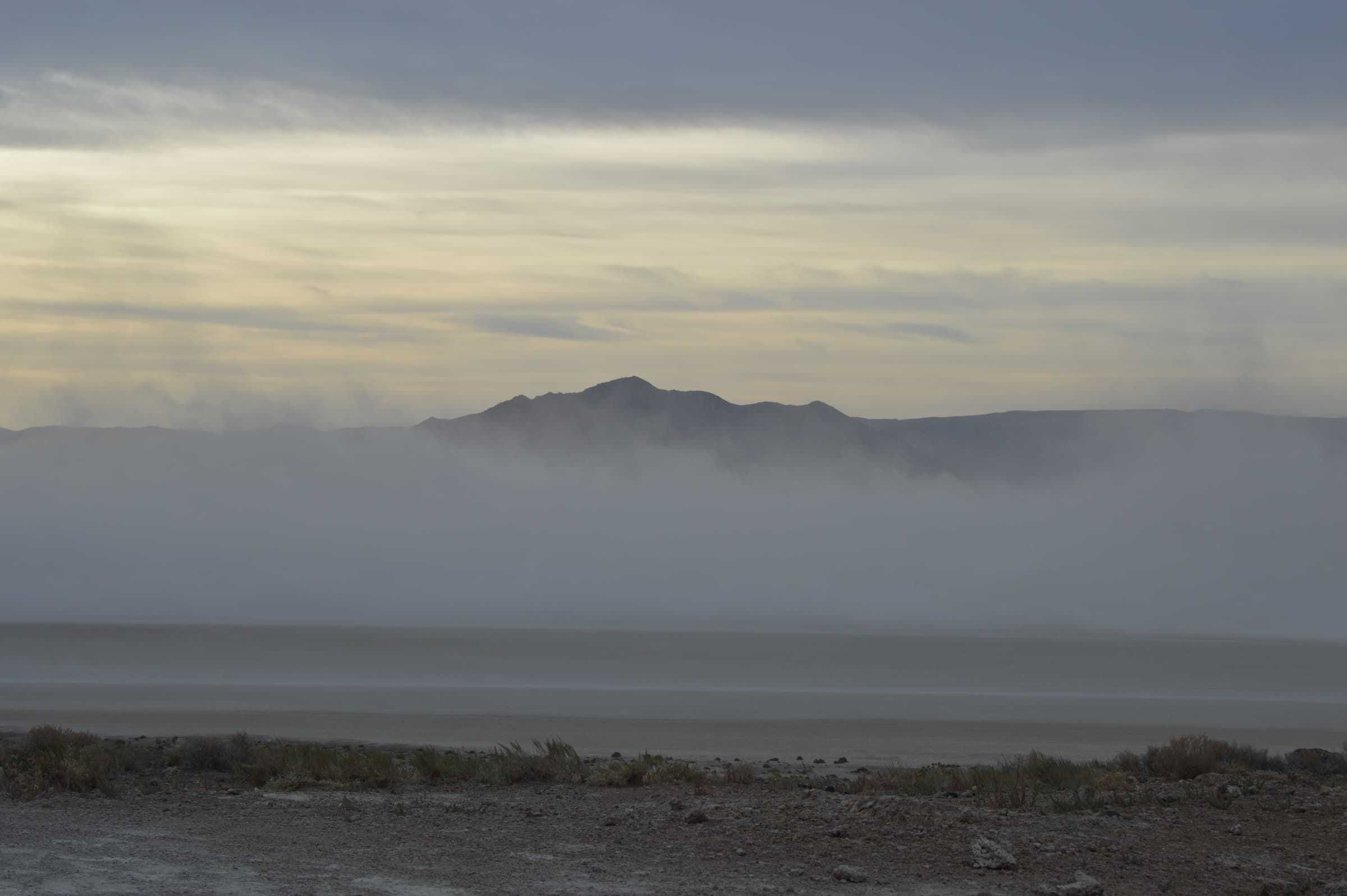 A dust storm moving across the open Black Rock Desert playa under a bright, breaking sky.