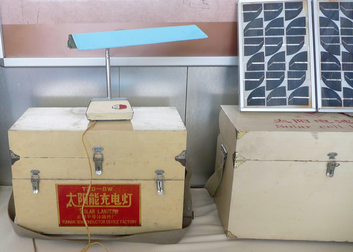 A solar lantern with a top handle and a panel on the lid, outdoors.