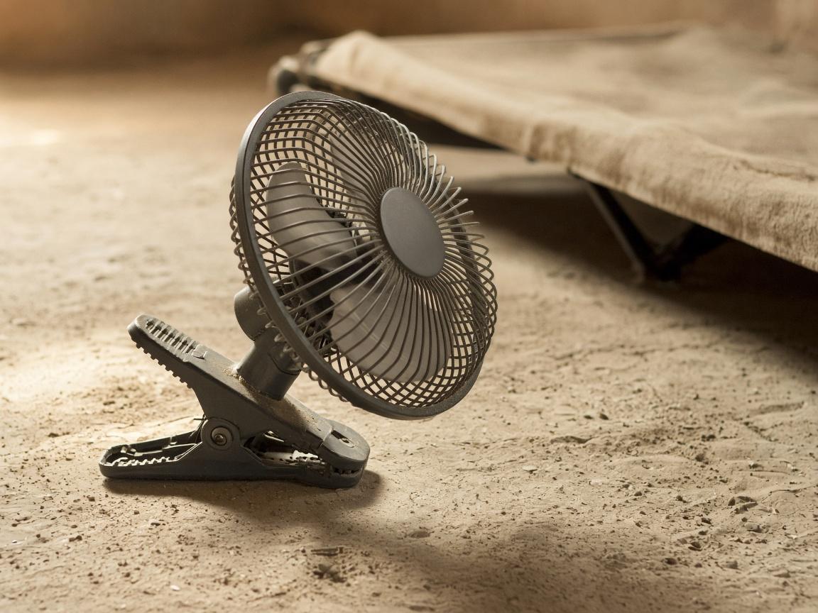 A rechargeable fan with a clamp, on pale dust under shade.