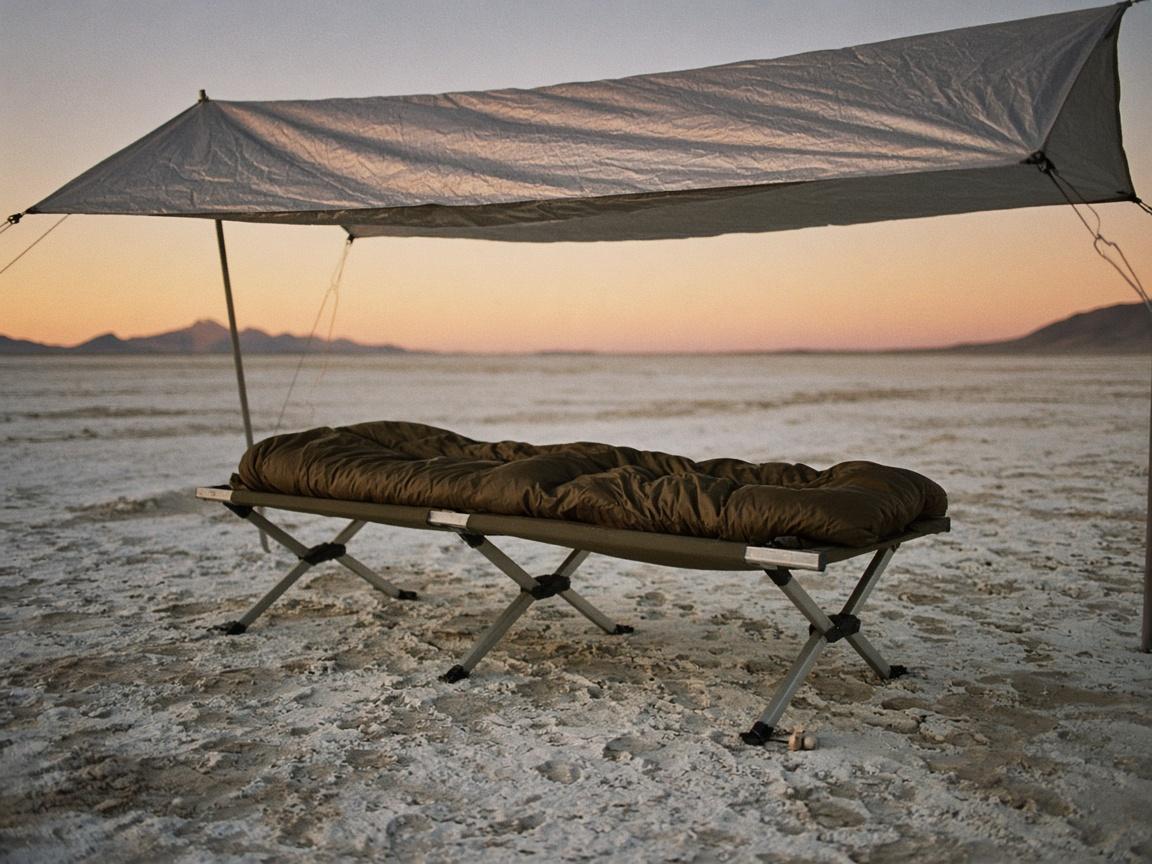 A camp cot and sleeping bag under shade, with earplugs on the frame.