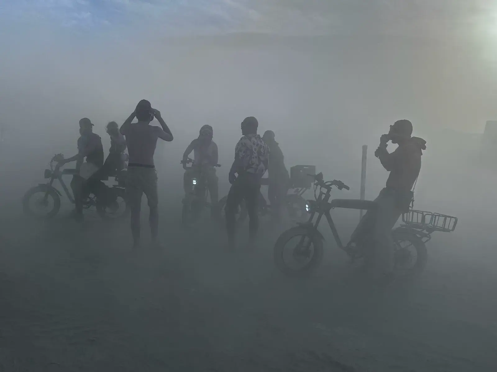 Dark silhouettes of people and bicycles in a white dust cloud, one bicycle with a round mirror.