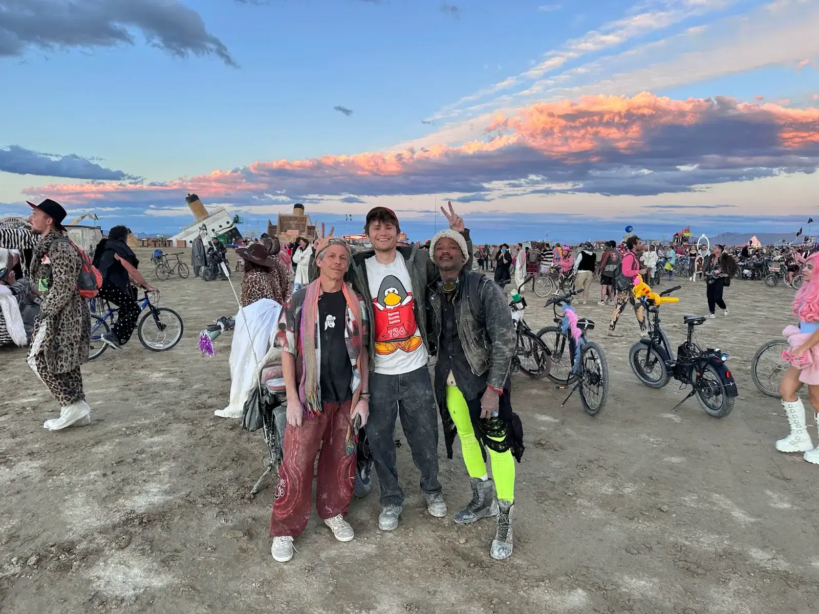 A group of people with bicycles in warm sunset light and blowing dust, several wearing hats and goggles.